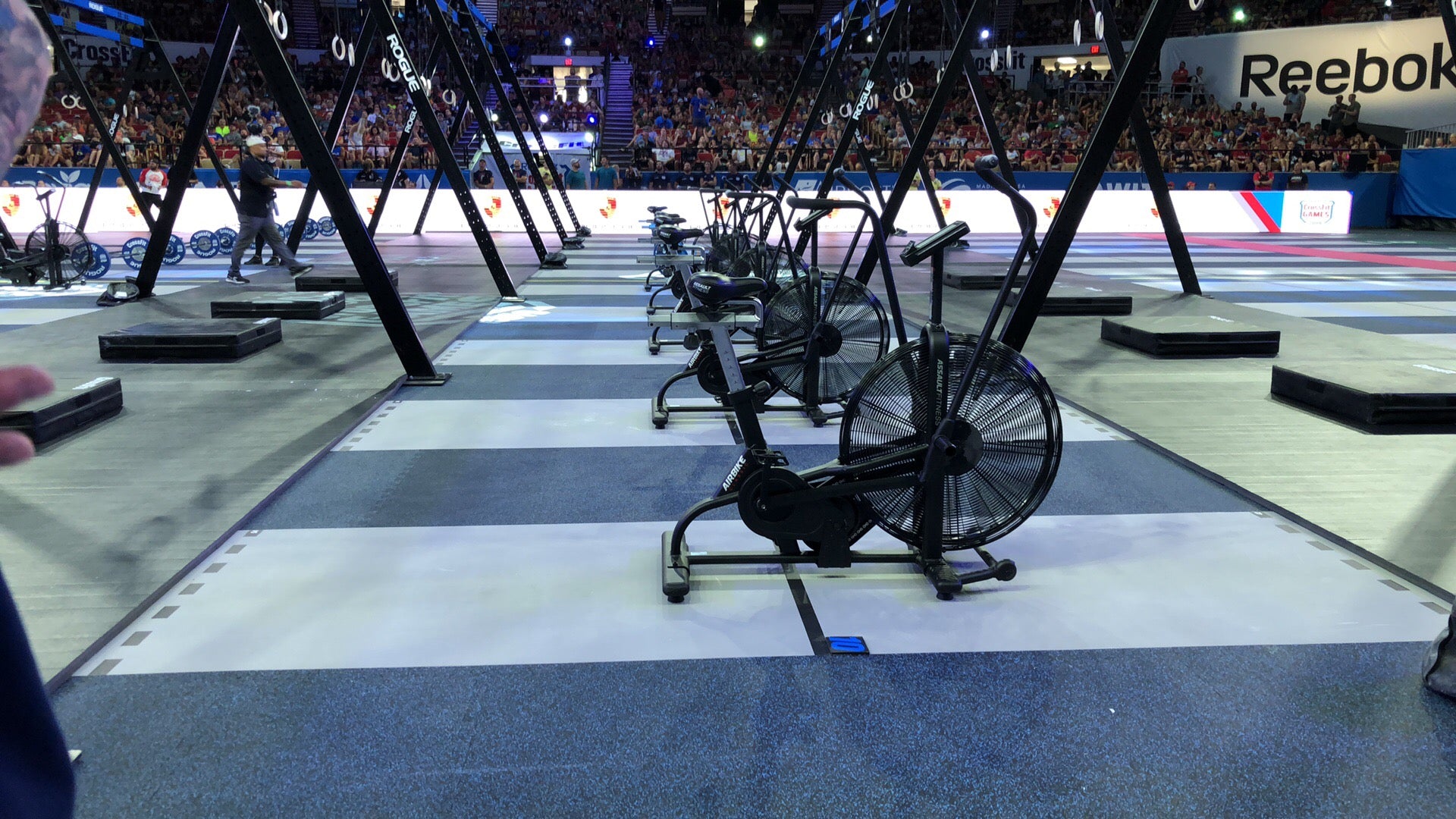 A long row of assaultbikes among other fitness equipment in an arena competitive setting