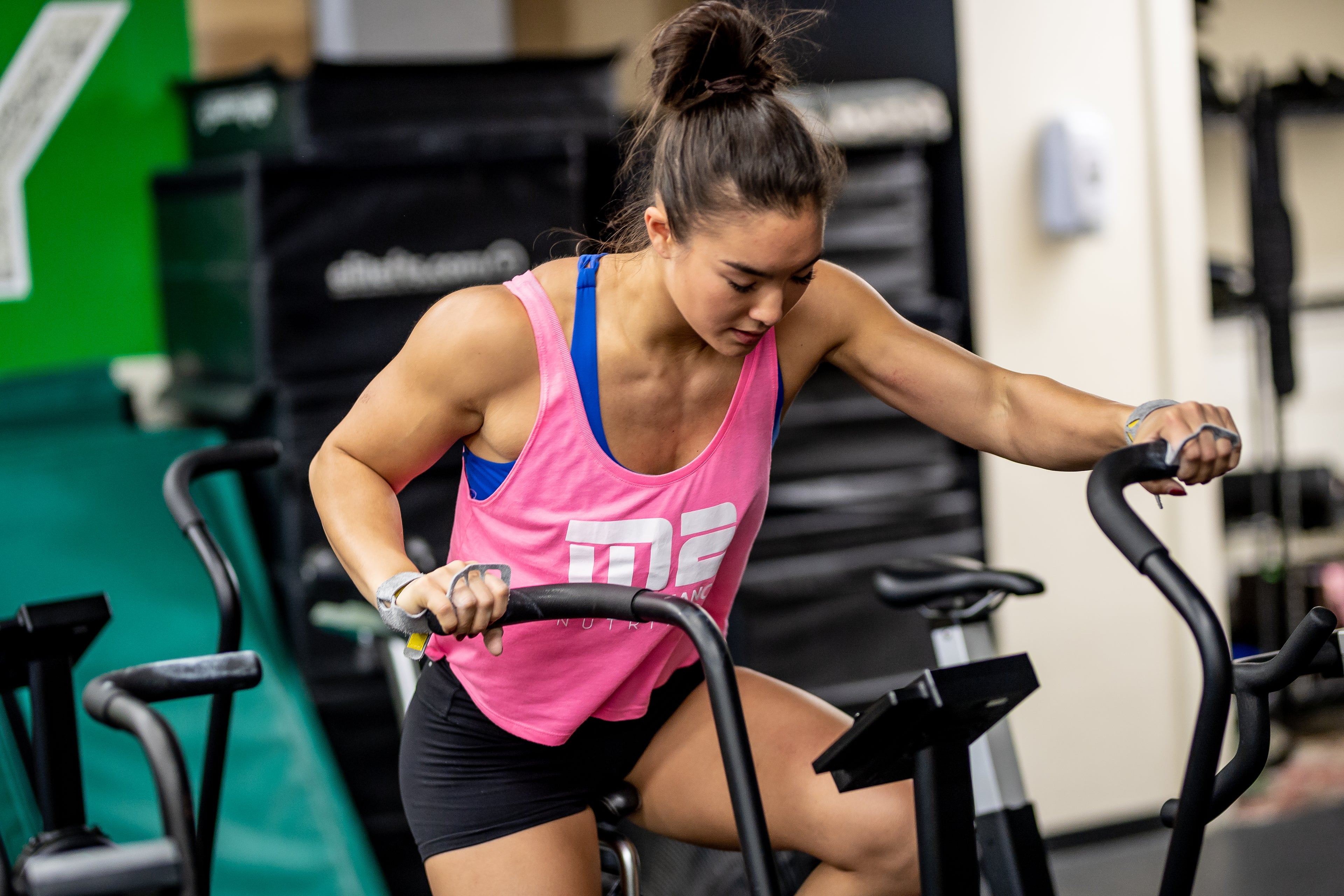 Person in a pink shirt working out on the Assaultbike around other fitness equipment